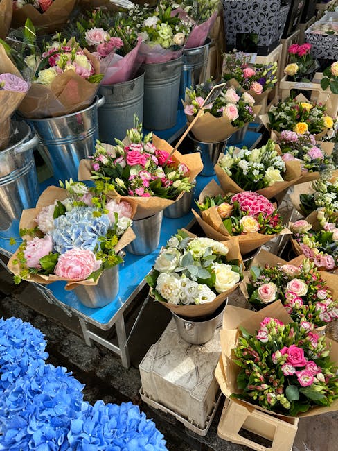 A vibrant display of freshly arranged floral bouquets on a blue table at Tooting Flowers, featuring a variety of flower types including pink roses, white hydrangeas, pink carnations, and green foliage